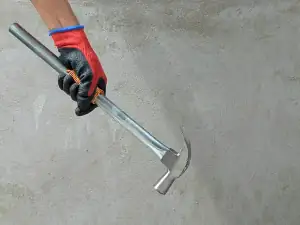 Gloved hand holding a chisel against concrete